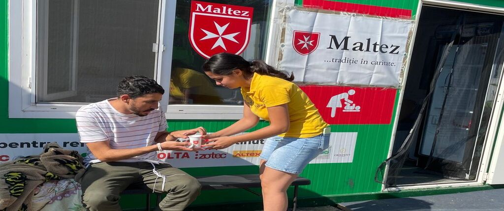 Mann erhält Getränk von einer Freiwilligen vor Malteser Container
